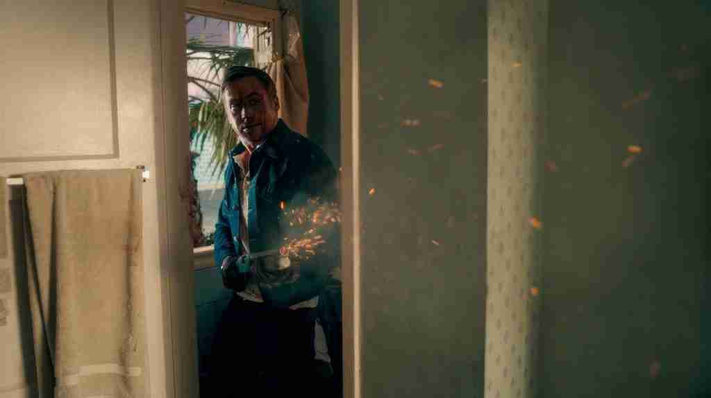 Drive beat sheet Act Two Part A motel shootout: Ryan Gosling as Driver fires shotgun at assassin through doorway with sparks flying in intense fight scene