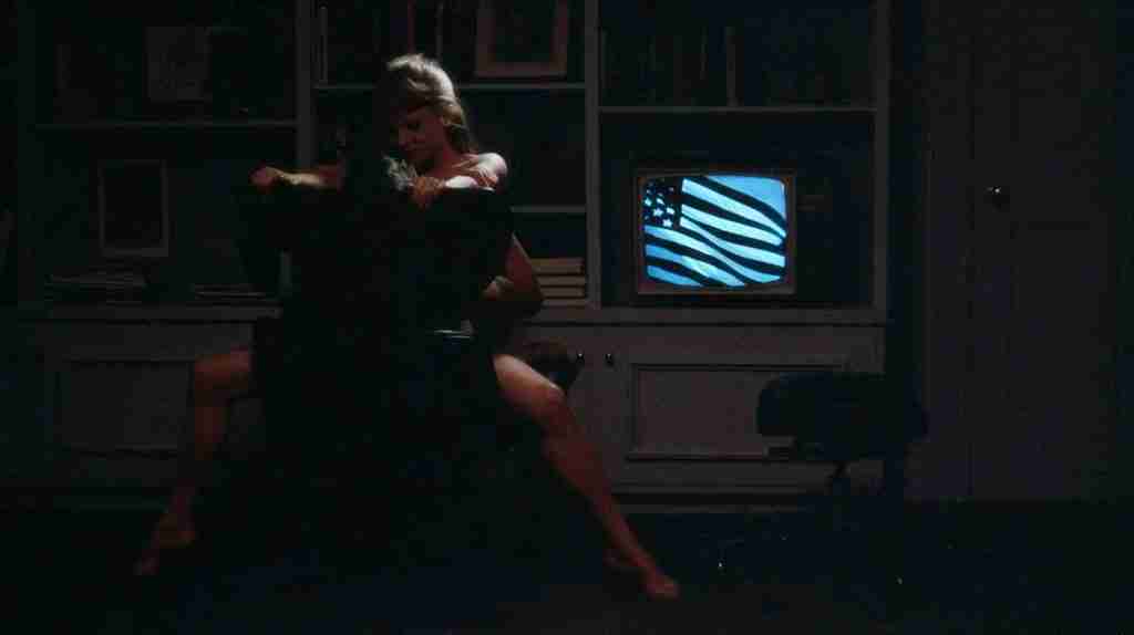 Joel and Lana in the chair sex scene with an American flag on the TV, representing capitalist satire in a Risky Business breakdown.