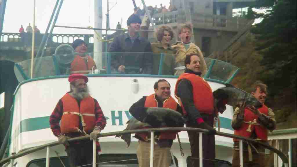 Patients from One Flew Over the Cuckoo's Nest triumphant on the boat deck holding large caught fish, including McMurphy and the group in orange life vests, returning to the dock after their liberating deep-sea fishing adventure (1975)