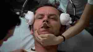Jack Nicholson as R.P. McMurphy restrained during electroshock therapy in One Flew Over the Cuckoo's Nest (1975), with bite guard and headgear, showing institutional oppression
