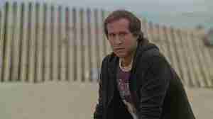 Fletch beat sheet featured image – Chevy Chase as Irwin Fletcher undercover on LA beach in zip-up hoodie and Lakers t-shirt 1985 movie opening scene