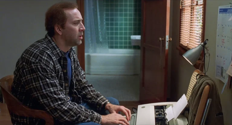 Nicolas Cage as Charlie Kaufman sits at a typewriter beside a window in Adaptation (2002).