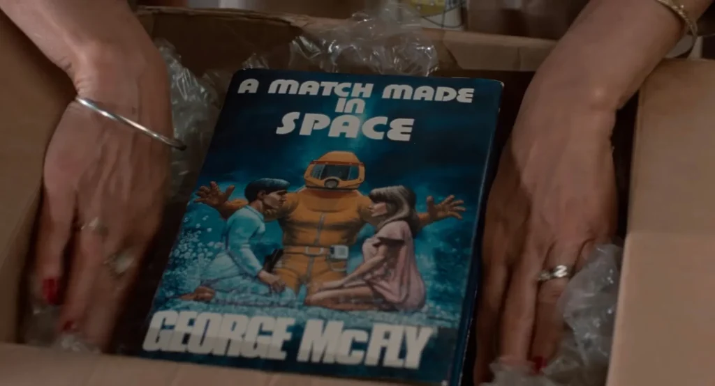 Hardcover novel titled A Match Made in Space by George McFly showing a figure in an orange suit between a man and a woman, Back to the Future foreshadowing payoff