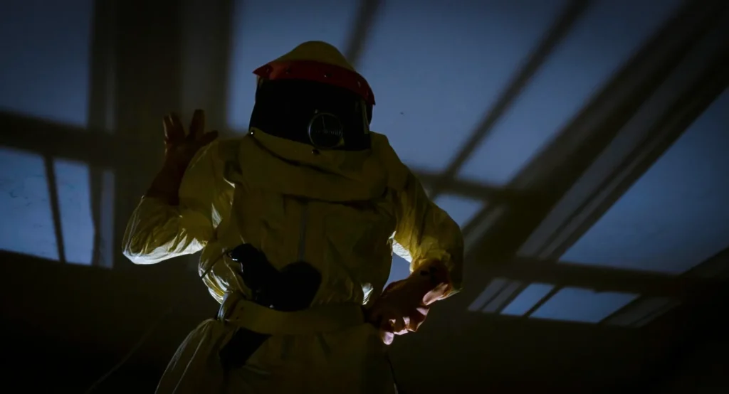 Figure in a yellow radiation suit and dark visor standing in a darkened bedroom, Back to the Future foreshadowing