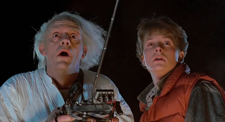 Doc Brown holding a remote control beside Marty McFly, both looking up in shock at night, setups and payoffs in Back to the Future