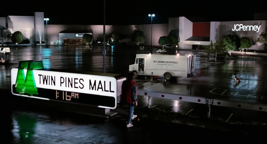 Twin Pines Mall sign with a two-tree logo in a rainy parking lot at night, setups and payoffs in Back to the Future