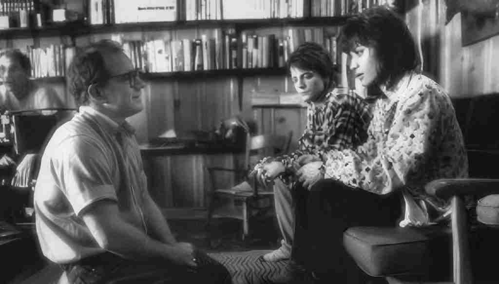 Black and white behind-the-scenes shot of writer/director Paul Schrader talking intently with lead actors Michael J. Fox and Joan Jett.