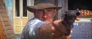 Indiana Jones aims a revolver, representing his reliance on human action and empirical skepticism, which is central to the film's structural paradox.