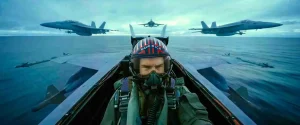 Tom Cruise as Maverick in an F/A-18 cockpit with three jets in formation over the ocean behind him
