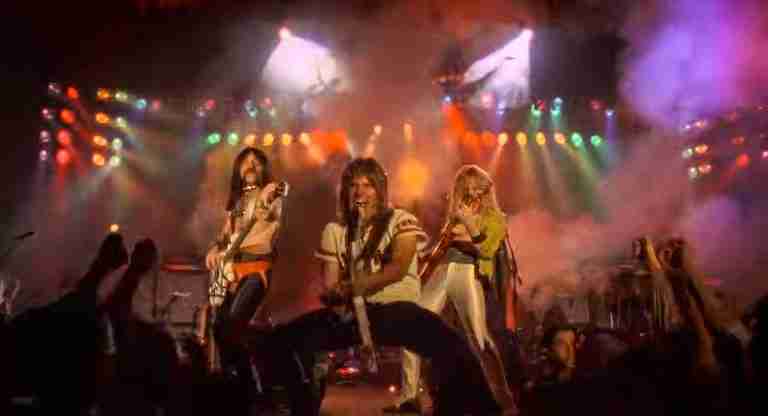 L to R: Harry Shearer as Derek Smalls, Christopher Guest as Nigel Tufnel, and Michael McKean as David St. Hubbins rocking out on stage with guitars, dramatic colorful lights, and smoke during the final reunion concert scene in Rob Reiner's mockumentary This Is Spinal Tap.