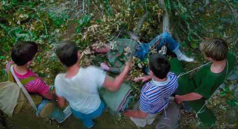 Stand By Me analysis featured image: Overhead view of Gordie, Chris, Teddy, and Vern standing around Ray Brower's body in the woods.