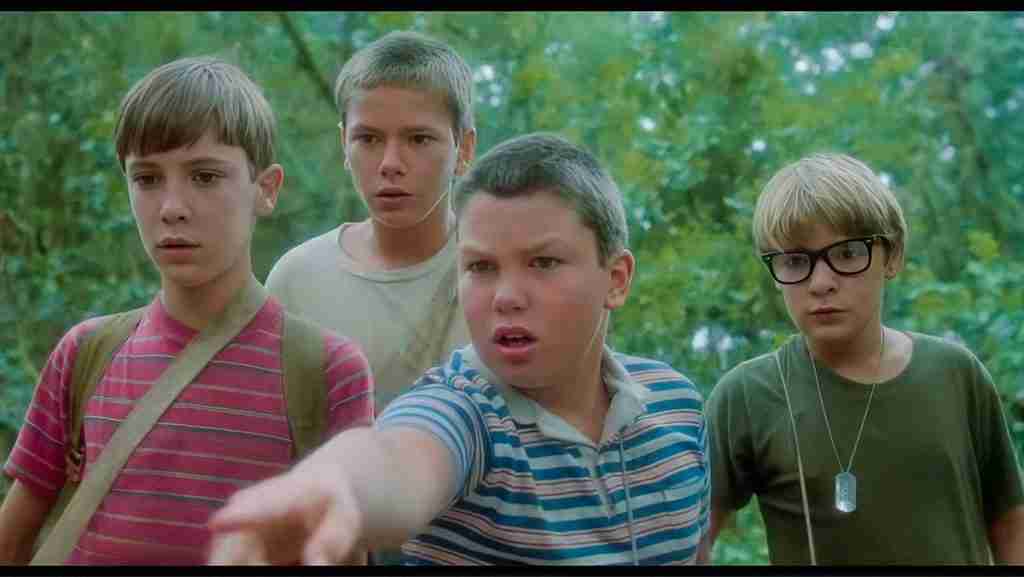 Stand By Me analysis: Gordie Lachance, Chris Chambers, Teddy Duchamp, and Vern Tessio standing together in the woods, with Vern pointing ahead excitedly.