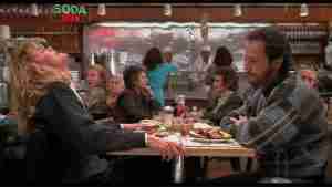 Meg Ryan tilts her head back in exaggerated fake orgasm at Katz's Deli table, while Billy Crystal watches in surprise; older woman in background points and delivers the famous line.