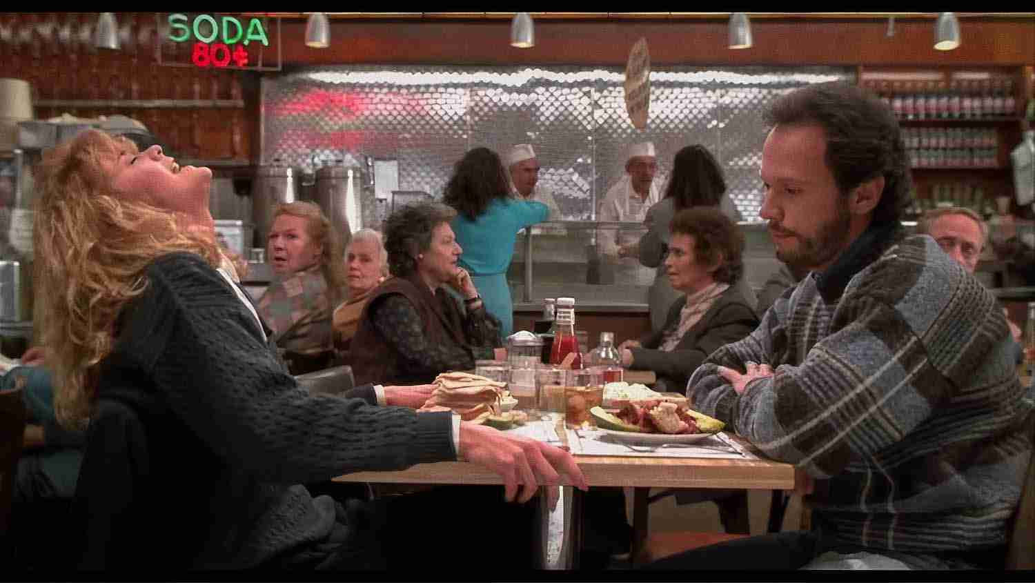 Meg Ryan tilts her head back in exaggerated fake orgasm at Katz's Deli table, while Billy Crystal watches in surprise; older woman in background points and delivers the famous line.
