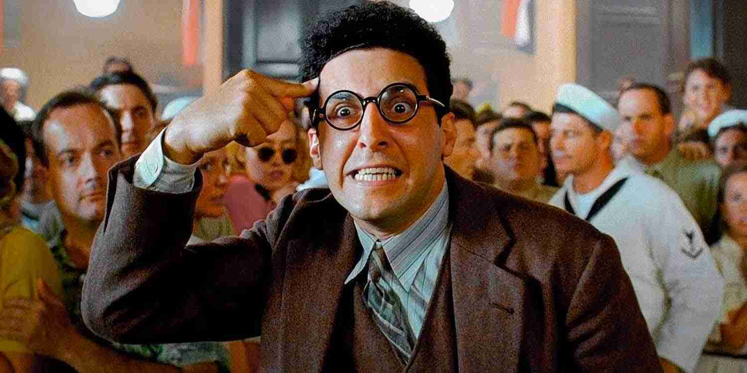 John Turturro as Barton Fink, in glasses and a suit, points frantically at his head in a crowded room, symbolizing the intense creative conflict in the screenwriter vs producer vision debate.