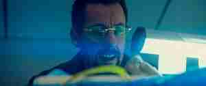 Adam Sandler as Howard Ratner in Uncut Gems, bathed in blue light while obsessively inspecting the black opal.