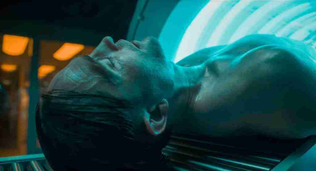 Mickey 17 analysis tension section image: Robert Pattinson as Mickey Barnes lying in cloning printer machine with blue glow, representing reprinting and expendable conflict