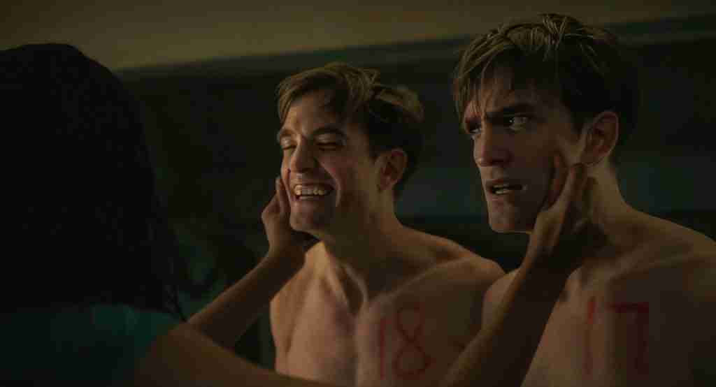 Mickey 17 analysis meet the cast image: Robert Pattinson as Mickey 17 and 18 shirtless with red numbers marked, laughing and touching faces while Nasha watches, illustrating clonal identity and arcs