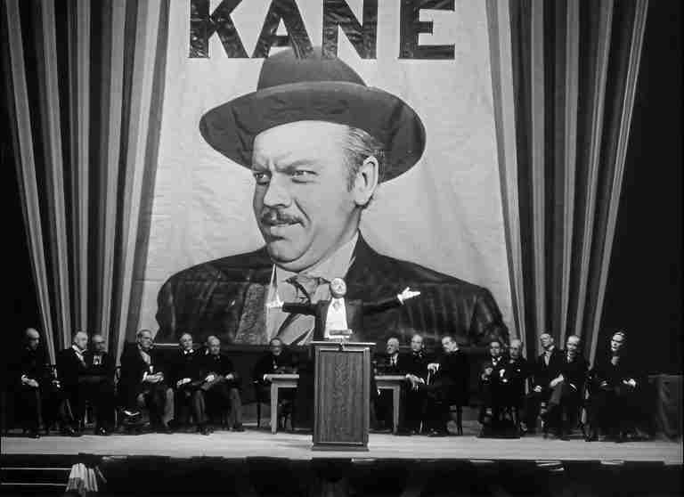 Charles Foster Kane on massive campaign banner during rally in Citizen Kane, symbolizing his peak power and cult of personality