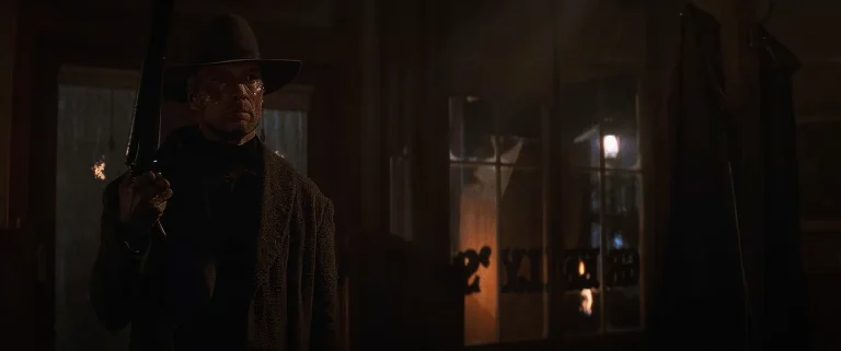 Clint Eastwood as William Munny holding a shotgun inside Greely's saloon at night in Unforgiven (1992)