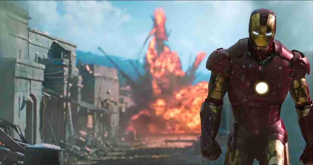 Iron Man in the red and gold Mark III armor walking away from a massive tank explosion in Gulmira.