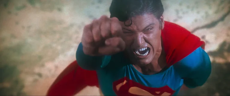 Christopher Reeve's Superman screaming in fury, fist raised, flying low over cracked, fissured ground in Superman (1978).
