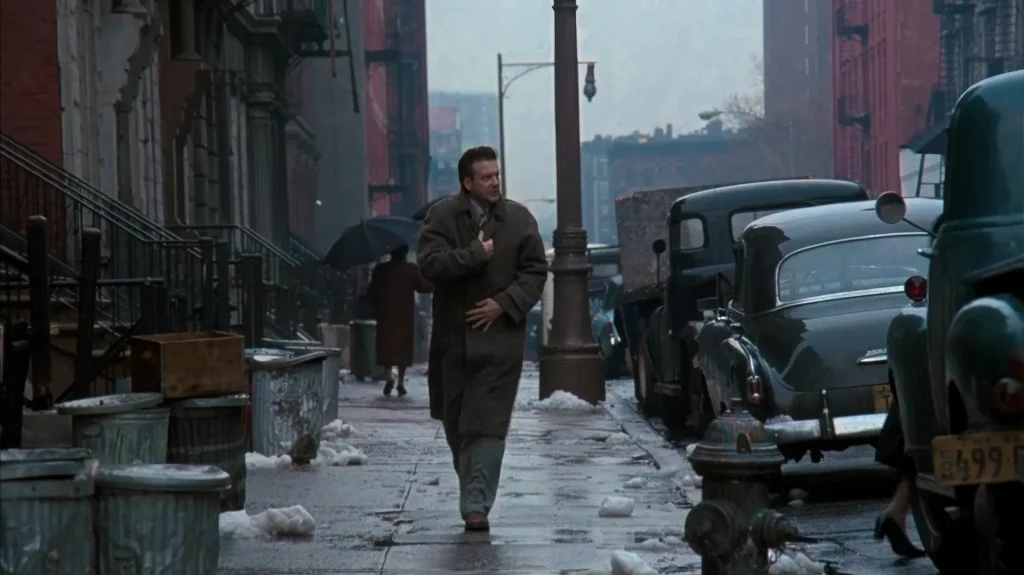 Angel Heart analysis — Mickey Rourke as Harry Angel walking through a snow-lined 1955 Harlem street on his way to meet Louis Cyphre at the Kingdom Mission, showing Alan Parker's drained color palette and period production design