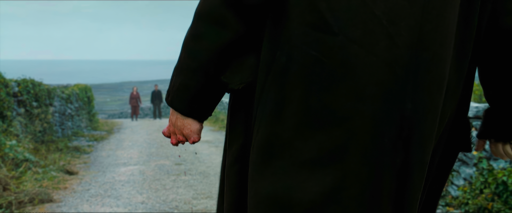 Close-up of Colm's bloody left hand missing all fingers in The Banshees of Inisherin, with Pádraic and Siobhán visible in the background on the road