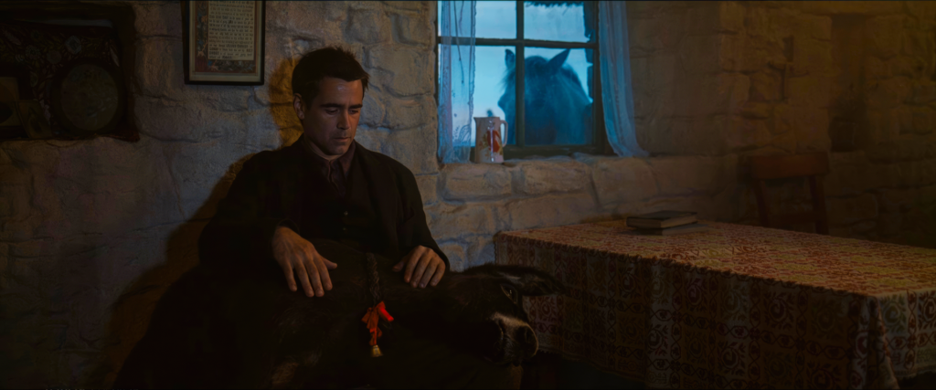 Pádraic sits with his dead miniature donkey Jenny on his lap while a horse watches through the window in The Banshees of Inisherin
