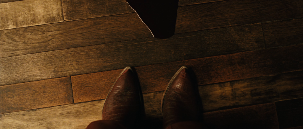 Anton Chigurh lifts his boots onto the motel bed as Carson Wells's blood advances across the floor, while on the phone with Llewelyn Moss in No Country for Old Men.