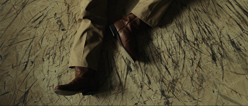 The deputy's boot scuff-marks on the polished hardwood floor of the Terrell County sheriff's office after Anton Chigurh strangles him with handcuffs in the opening scene of No Country for Old Men.