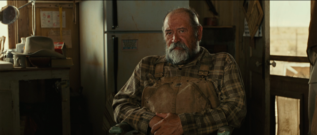 Uncle Ellis seated in his West Texas cabin, played by Barry Corbin in the Coen brothers' adaptation of No Country for Old Men, the scene where he tells Sheriff Bell that the country has always been hard on people