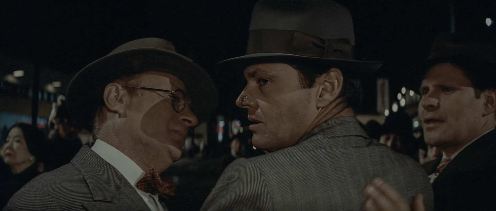 Jake Gittes, a bandage across his nose, stands face to face with Walsh in wire-rim glasses on a dark Chinatown street as Duffy looks on