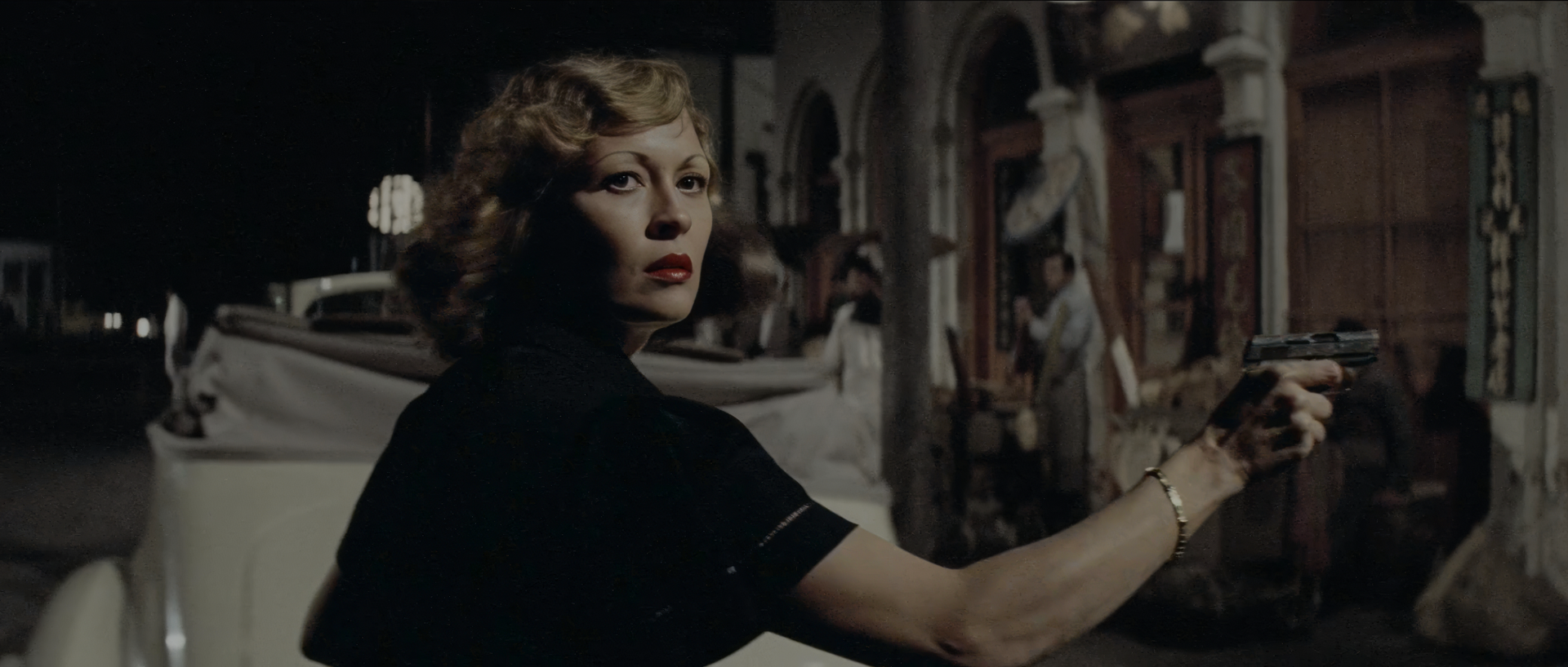 aye Dunaway as Evelyn Mulwray at night on a Chinatown street, looking back over her shoulder in a black dress and red lipstick, pointing a pistol off-frame beside a white convertible.