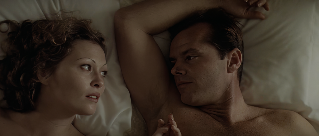 Overhead shot of Faye Dunaway as Evelyn Mulwray and Jack Nicholson as Jake Gittes lying in bed in Chinatown, facing each other on white sheets, her hand resting on his chest, the stitches visible on his nose.