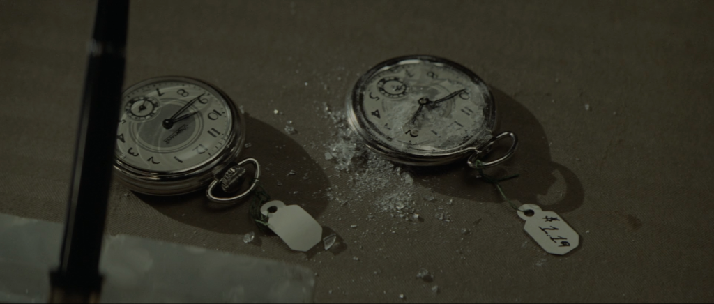 Two cheap pocket watches on a surface, one intact and one crushed with its glass shattered and a $1.19 price tag, in Chinatown.
