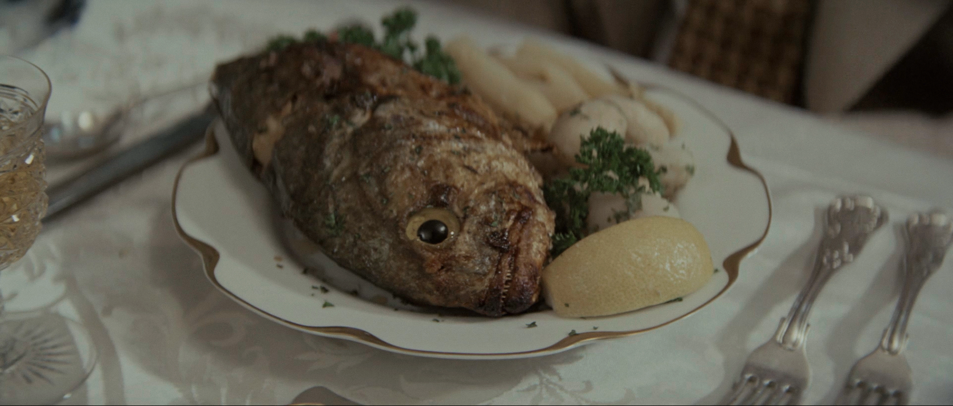 A whole cooked fish served on a china plate with its eye intact, beside boiled potatoes and a lemon wedge, at Noah Cross's lunch table in Chinatown.