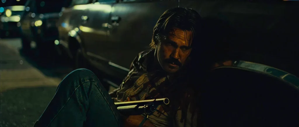 Llewelyn Moss bloodied behind a car with the sawed-off shotgun during the Eagle Pass street shootout in No Country for Old Men