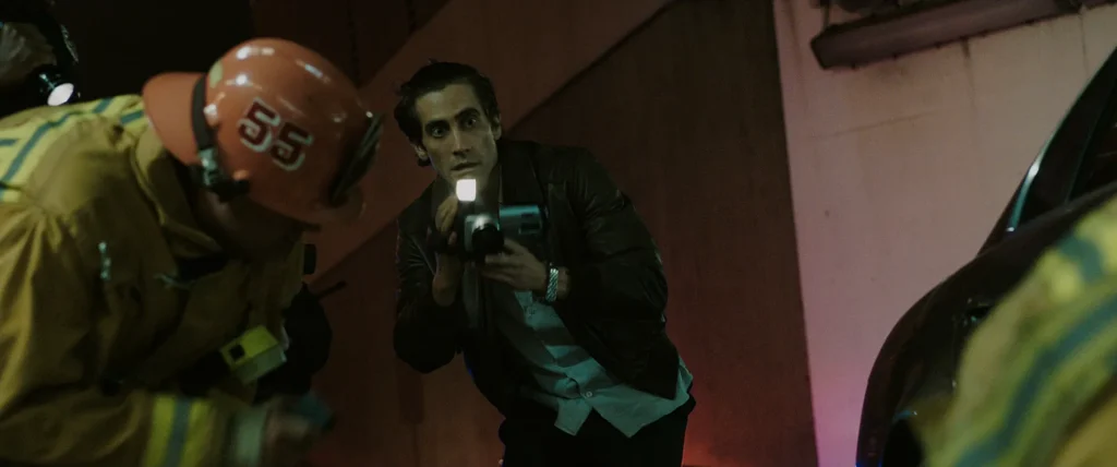 Lou Bloom aims a camcorder light at firefighters working a nighttime scene in Nightcrawler.
