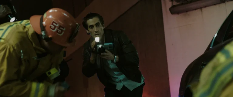 Lou Bloom aims a camcorder light at firefighters working a nighttime scene in Nightcrawler.