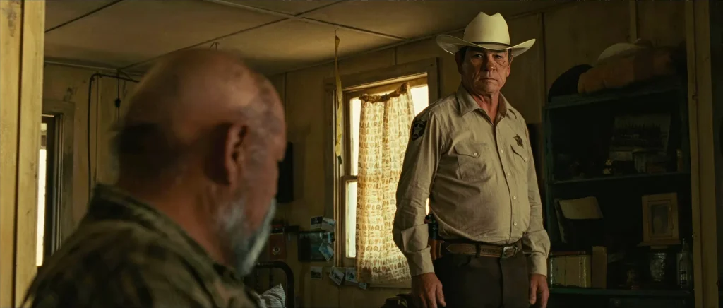 No Country for Old Men book vs movie: Sheriff Bell (Tommy Lee Jones) standing in Ellis's cabin, the scene where the novel's wartime confession was cut from the film