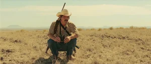 No Country for Old Men book vs movie: Llewelyn Moss (Josh Brolin) crouched in the West Texas grassland, the landscape the film opens on instead of the screenplay's snow