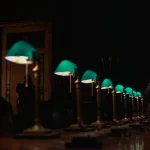 Arthur Jensen (Ned Beatty) standing at the end of a long dark boardroom table lined with green banker's lamps in Network (1976)